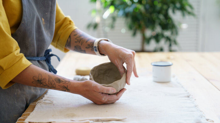 Creating Pottery: Table In Ceramic Studio With Master Hands Shaping Clay Pot. Woman Potter Sculpting